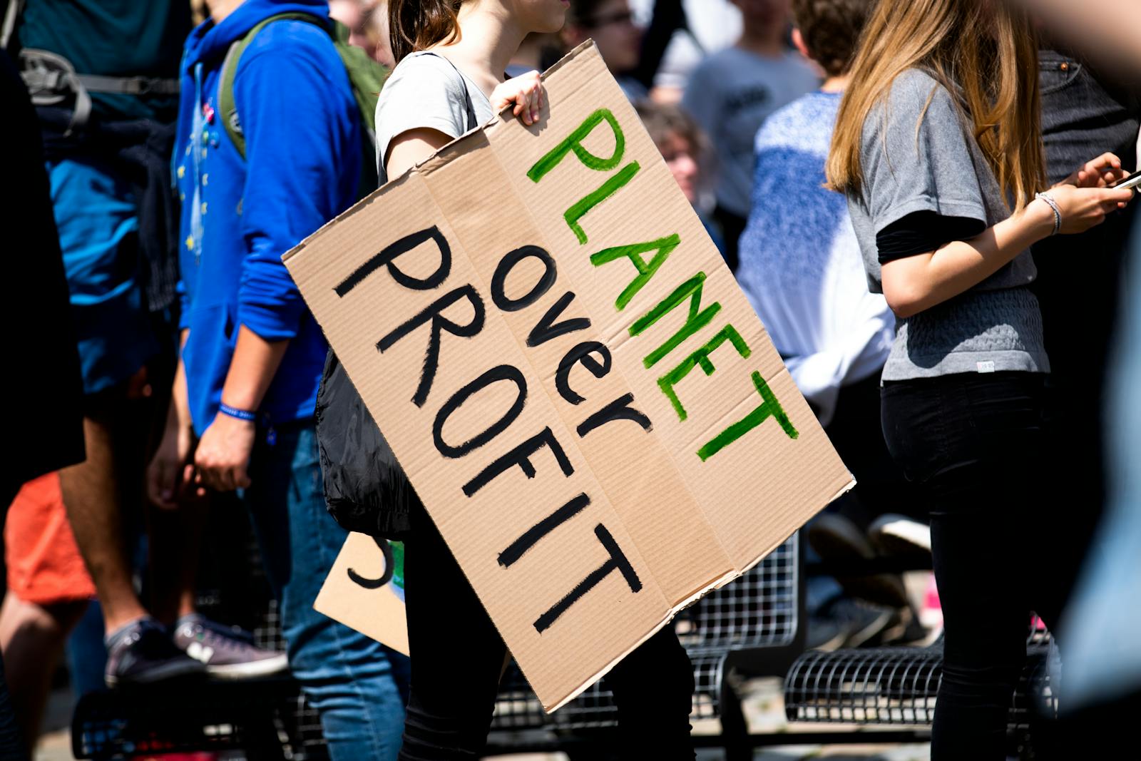 Planet over profit Youth climate protest with participants holding 'Planet Over Profit' sign.